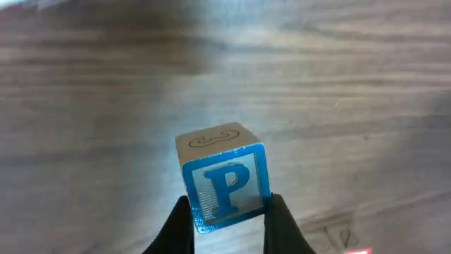 The left gripper holds the P block. The wrist camera looks down on its top face, the letter P, and past it onto a side face with a 3.